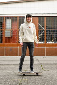A model stands on a skateboard with a warehouse behind him wearing the Bear Hoodie.