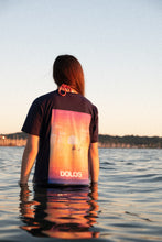 Load image into Gallery viewer, A model poses facing away from the camera, waist-deep in water with the Navy Sunset Surfer Tee.