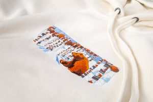 A close up of the design on an off-white hoodie. The design includes a brown bear in a snowy forest.