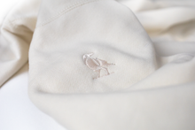 Load image into Gallery viewer, A close up of off-the white Dolos bird embroidered on the right shoulder.
