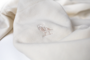 A close up of off-the white Dolos bird embroidered on the right shoulder.