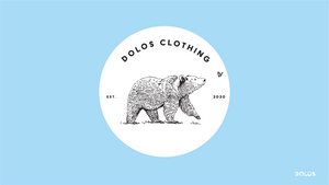 View from the front - A white sticker with a black bear happily following a butterfly. The sticker says Dolos Clothing on top, and Est. 2020 on the sides