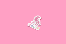 Load image into Gallery viewer, View from an angle - A white outlined sticker with the pink Dolos Bird on it. Below the bird it says Dolos in a colorful font.
